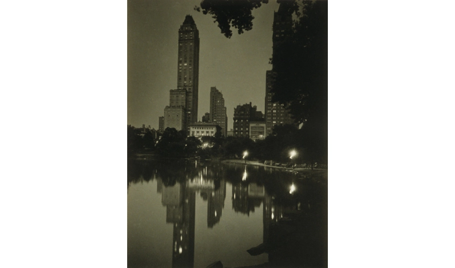 Photo of Central Park at night with a reflection of buildings in the background in the water in the foreground